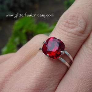 May include: A silver ring featuring a large, cushion-cut, deep red gemstone. The ring has a split shank design, with two parallel bands. The website address www.glitterfusion.etsy.com is visible in the image.