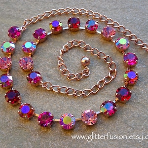 May include: A rose gold necklace featuring a series of iridescent, round, magenta-colored crystals. The crystals are set in a delicate chain, with a matching clasp. The necklace is designed in a spiral shape.