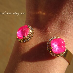 May include: Gold cuff bracelet with two large pink gem stones surrounded by clear rhinestones.