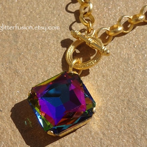Op de afbeelding: Een gouden ketting met een toggle sluiting en een grote, vierkante, iriserende edelsteen hanger.