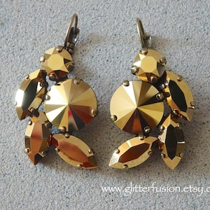 May include: A pair of gold-toned chandelier earrings. Each earring features a cluster of faceted, golden-yellow crystals in various shapes, including round and marquise. The earrings have a lever-back closure and are set against a light gray background.