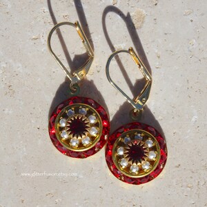 May include: A pair of gold earrings with red and white round glass beads. The earrings have a gold hook closure.