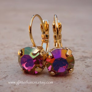 May include: A pair of gold hoop earrings with iridescent purple gemstones. The earrings have a simple design and are perfect for everyday wear.