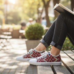 Puede incluir: Zapatillas de lona con un estampado geom&eacute;trico en rojo, blanco y negro. Los zapatos de corte bajo tienen cordones blancos y se usan con vaqueros oscuros. Los zapatos est&aacute;n en un banco de madera al aire libre.