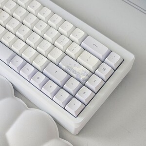 May include: A white mechanical keyboard with a light blue and white keycap featuring a cloud design. The keyboard has a minimalist design with a white frame and white keys.