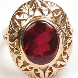 Puede incluir: Un anillo de oro con una gran piedra roja ovalada engastada en un diseño de filigrana.