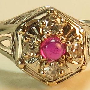 May include: A vintage ring with a pink ruby surrounded by small diamonds set in a gold filigree design.