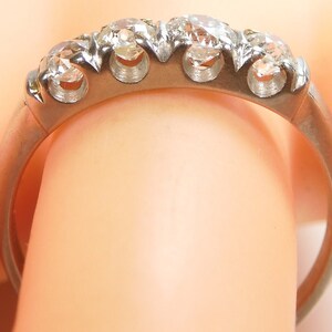 Puede incluir: Un anillo de banda de plata con cinco diamantes redondos engastados en garras. El anillo est&aacute; en un dedo.