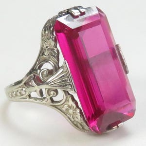 May include: A vintage ring with a large, rectangular, pink gemstone set in a filigree silver band.