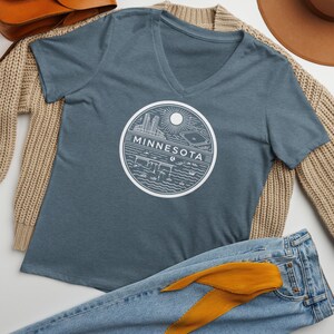 May include: A blue V-neck t-shirt with a white graphic of a cityscape and the word "MINNESOTA" in a circle.