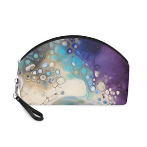 May include: A half-circle shaped cosmetic bag with a zipper closure and a black strap. The bag is printed with a colorful abstract design featuring swirls of blue, purple, and white with a pattern of small circles.