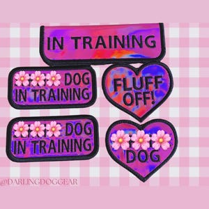 May include: Dog training patches in pink and purple with text. Rectangular patches read "IN TRAINING". Heart-shaped patches say "FLUFF OFF!" and "DOG". Floral accents are included.