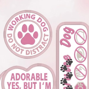 Puede incluir: Un conjunto de parches de San Valentín con diseños bordados en rosa. Incluye un parche redondo con una huella de pata y el texto "Do Not Distract Working Dog", un parche en forma de corazón con texto y un parche rectangular con huellas de patas y la palabra "Dog".