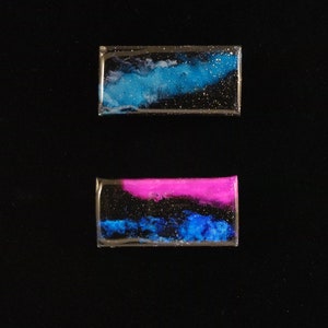 Handpainted nebula magnet set, nebula magnet set, one primarily blue and the other pink and blue covered and resin, painted in gold on the back and initialled with date.