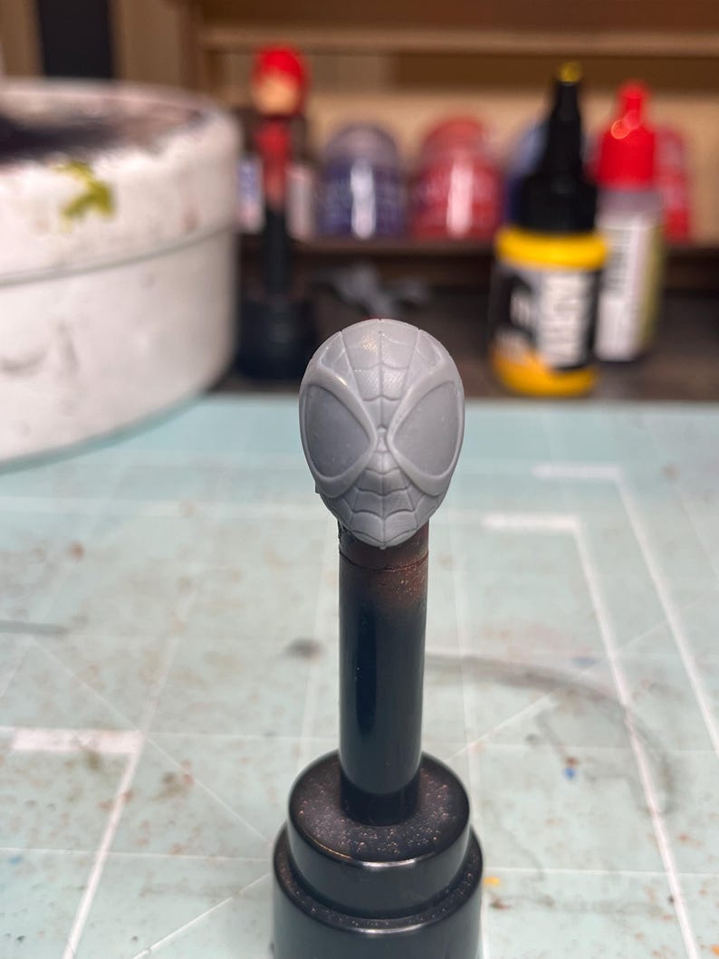 May include: A gray plastic unpainted head sculpt of a superhero with a spider web design on the mask.