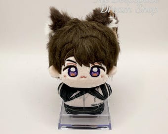 Puede incluir: Muñeco de peluche con pelo castaño, orejas de gato y un atuendo blanco y negro. El muñeco tiene grandes ojos morados y se exhibe sobre un soporte transparente. El texto "The Deepspace Dream Shop" es visible en el fondo.