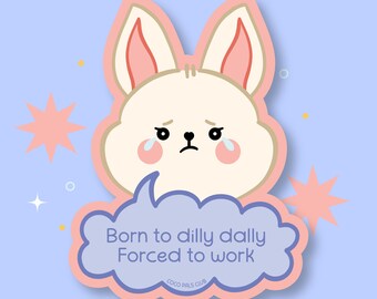 May include: A sticker featuring a cartoon bunny with a sad expression, tears, and rosy cheeks. The bunny is cream-colored with pink accents and a light blue background. Text in a speech bubble reads "Born to dilly dally Forced to work."