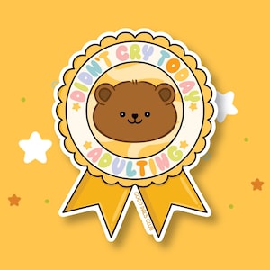 May include: A sticker with a cartoon bear face in a circular badge design. The badge reads "Didn't Cry Today, Adulting" in pastel colors. The sticker has a yellow background with star and dot accents.