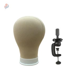 May include: A beige canvas wig head with a white base, next to a black clamp. The wig head is shaped like a human head and is used for styling and displaying wigs. The clamp is used to secure the wig head to a table or other surface.