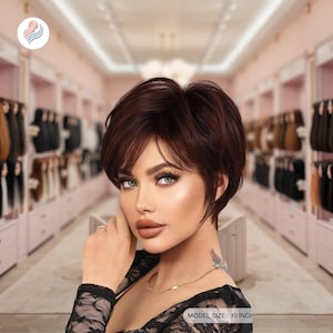 Puede incluir: Una peluca corta de color castaño rojizo con flequillo lateral. La peluca está peinada con un corte pixie y parece tener 25 cm de largo. El fondo muestra una tienda con varias pelucas.