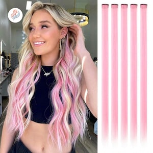 May include: A woman with blonde hair and pink highlights. To the right are five pink hair extensions with clips. The woman is wearing a black top and a necklace. The hair extensions are a solid, vibrant pink color.