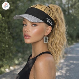 May include: A black visor with a white and black checkered underside and the word "Freedom" in white script. The visor is worn by a person with blonde hair pulled back in a ponytail.