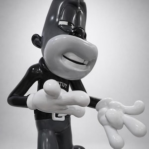 May include: A black and white statue of a cartoon character wearing a top hat, black suit, and white gloves. The character has a large white smile and the word "TUY" is visible on the collar.