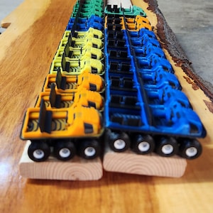 May include: A line of toy vehicles in various colours, including blue, yellow, orange, green, and red. The vehicles are arranged in a row on a wooden surface. Each vehicle has four wheels and a detailed design.