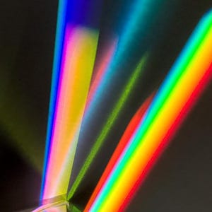 Pode incluir: Um close-up de um prisma refratando a luz, criando múltiplas faixas de cores como um arco-íris.