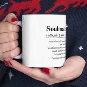 May include: White ceramic mug with a black definition of the word "Soulmate" printed on it. The definition reads: "{sol-mat} noun your other half in a relationship, you feel comfortable and connected, a match that just fits, bringing warmth. Destined to be together."
