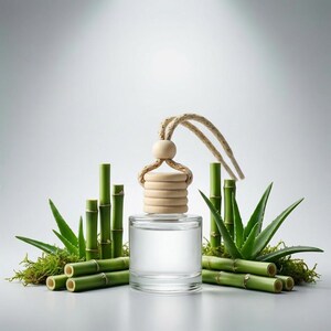 May include: A clear glass bottle with a wooden cap and a beige rope, surrounded by green bamboo stalks, aloe vera leaves, and moss. The bottle appears to contain a clear liquid, suggesting a fragrance or essential oil product. The overall aesthetic is natural and spa-like.