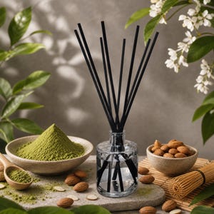 May include: A clear glass reed diffuser bottle filled with liquid and containing several thin black reeds. The diffuser is surrounded by a bowl of green matcha powder, a wooden scoop, a small bowl of almonds, and a bamboo whisk on a stone surface.
