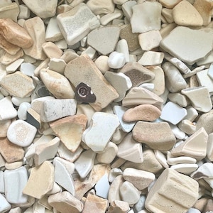 May include: A collection of irregularly shaped, neutral-toned stones and ceramic shards. The pieces vary in size and color, ranging from off-white to tan and brown. Some fragments have visible textures and patterns, creating a natural, earthy aesthetic.