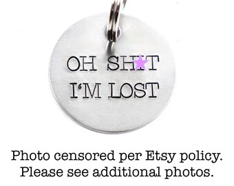 May include: A silver round dog tag with a key ring. The tag has the text "OH SHIT I'M LOST" with a purple star replacing the "I".