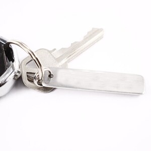 May include: A silver key chain with a silver key and a blank silver tag.