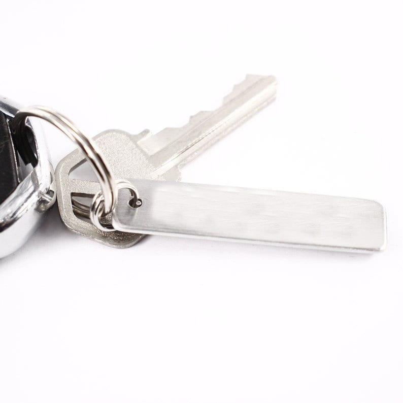 May include: A silver key chain with a silver key and a blank silver tag.