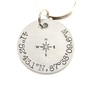 May include: Silver keyring with a compass design and coordinates engraved around the edge: 41°52'43.1"N, 87°38'09.6"W.