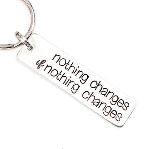 May include: Silver keyring with a rectangular tag that reads "nothing changes if nothing changes".