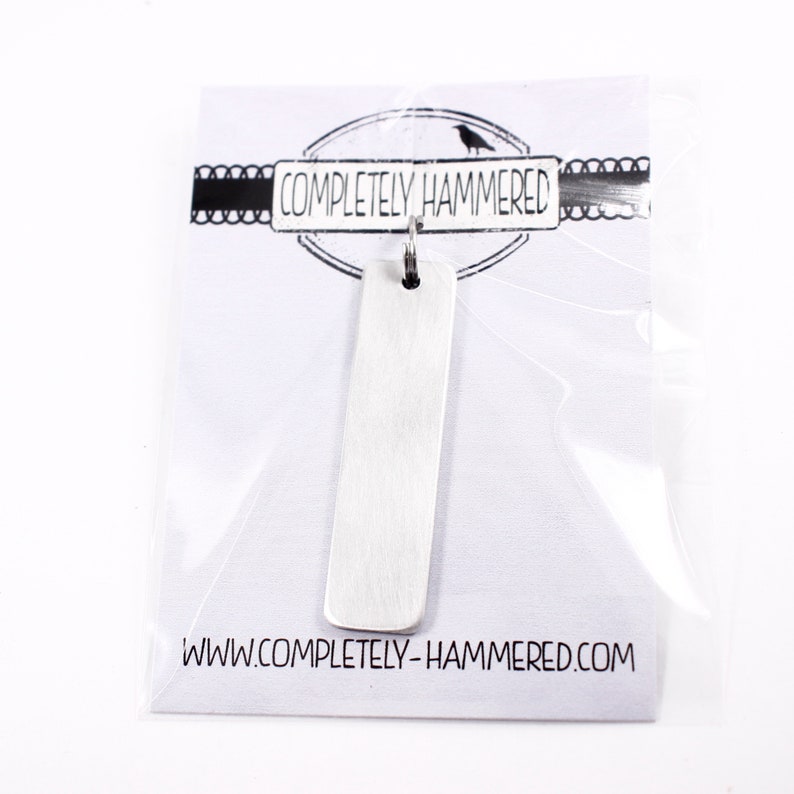 May include: A silver rectangular pendant with a hammered texture. The pendant is on a white card with the text "COMPLETELY HAMMERED" and a website address.