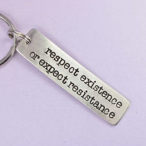 May include: Silver keychain with the text "respect existence or expect resistance" engraved on it.