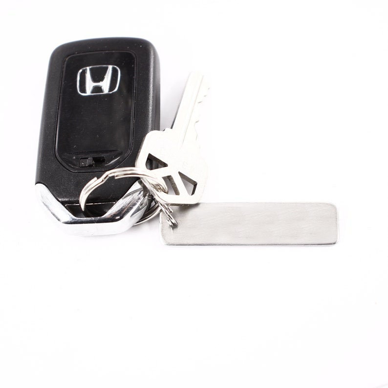 May include: A black car key with a silver key ring and a silver tag. The key has the Honda logo on it.