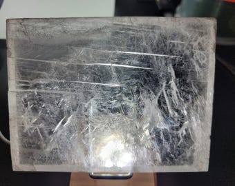 May include: A large, clear selenite crystal with a smooth, polished surface. The crystal has a translucent appearance and shows internal striations.