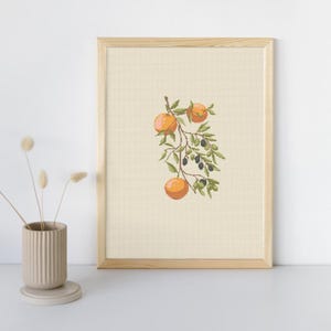 May include: A framed cross-stitch artwork featuring a branch with orange fruits and olive-like berries. The artwork is set against a cream-colored background and framed in light wood. A beige ceramic vase with dried flowers is in the foreground.