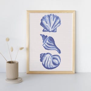 May include: A framed print featuring three blue seashell illustrations on a white background. The seashells are in a watercolor style, with varying shapes and details. The frame is made of light-colored wood.