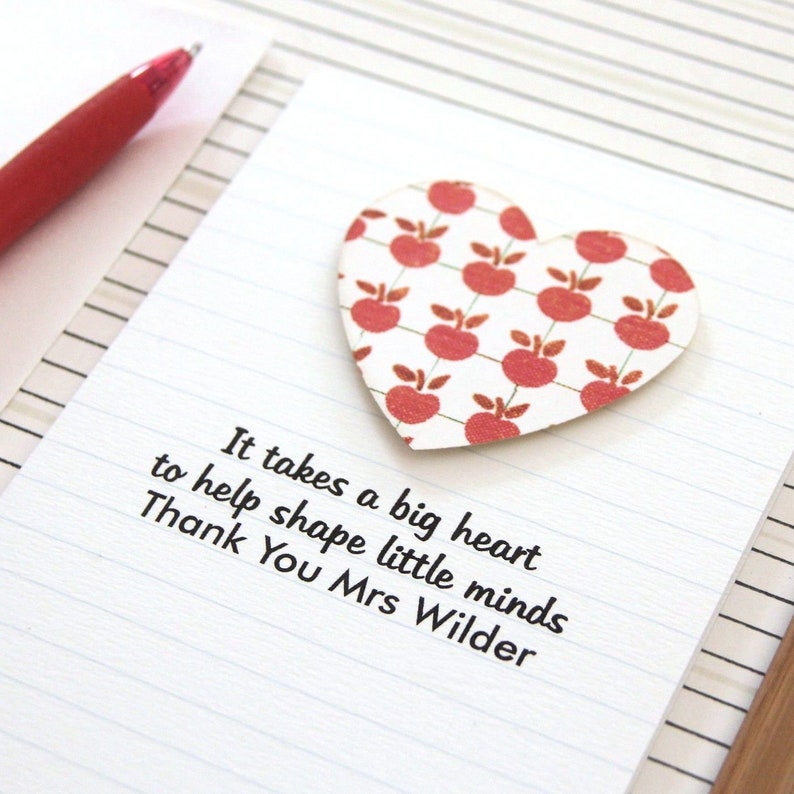 May include: A white card with lined paper and a red heart with a red apple pattern. The card has the text "It takes a big heart to help shape little minds Thank You Mrs Wilder".
