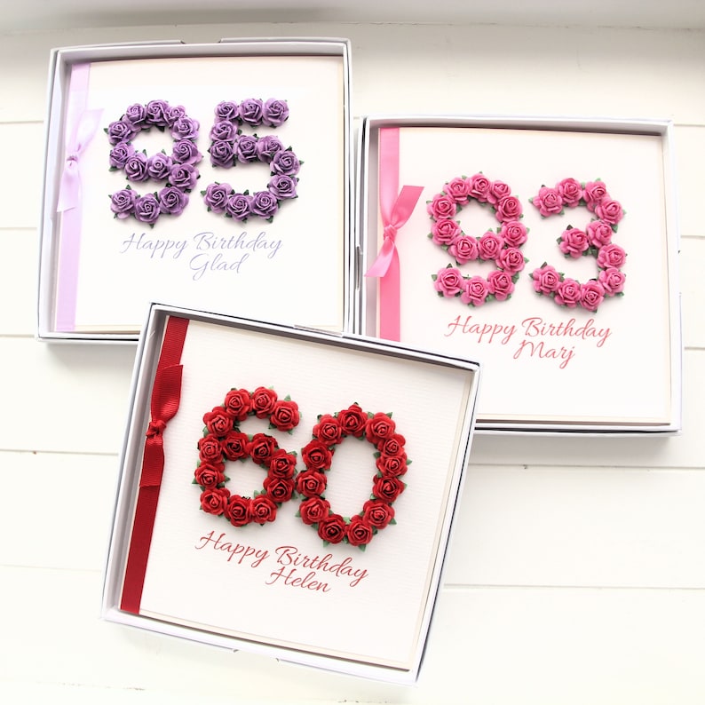 May include: Three birthday cards in white boxes. Each card features a number made of small roses. The numbers are 95 in purple, 93 in pink, and 60 in red. Each card has a ribbon and a birthday message.