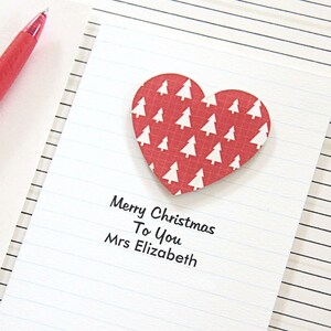 May include: A red heart-shaped card with a white Christmas tree pattern. The card has the text "Merry Christmas To You Mrs Elizabeth" written on it.