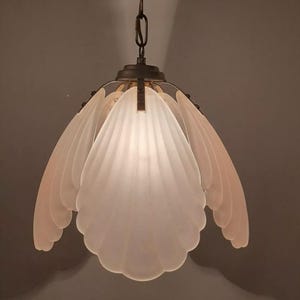 May include: A white frosted glass pendant light fixture with a chain hanging from the ceiling. The fixture is shaped like a flower with multiple petals.