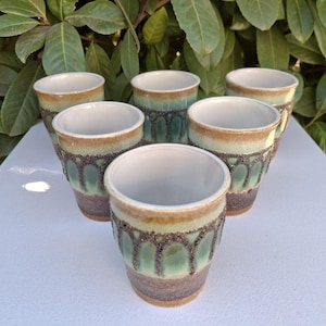 Peut inclure: Ensemble de six tasses en céramique avec un glaçage vert, brun et blanc. Les tasses présentent un design unique avec un motif d'arches répété.