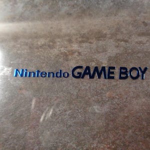 May include: A close-up of a light brown surface with the text "Nintendo GAME BOY" printed in blue.
